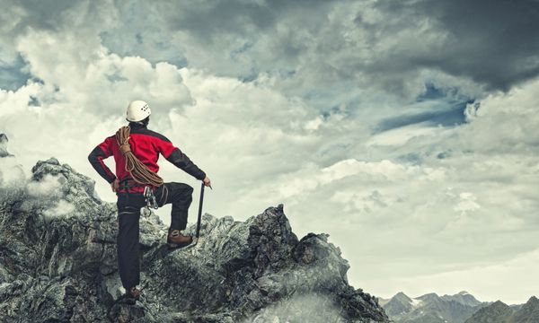 تصویر مرد جوان کوهنوردی که بالای صخره ایستاده است