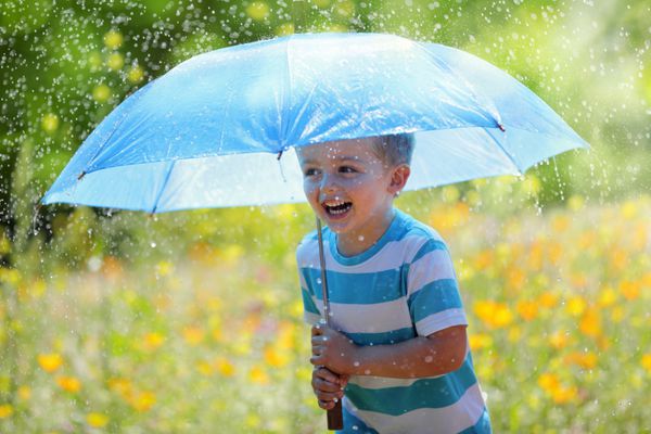 باران و آفتاب با پسری خندان که چتری در دست دارد و در چمنزاری از گل‌های وحشی می‌دوید