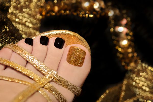 پدیکور لوکس با لاک مشکی و طلایی روی انگشتان پا زنانه در زمینه مشکی و درخشان