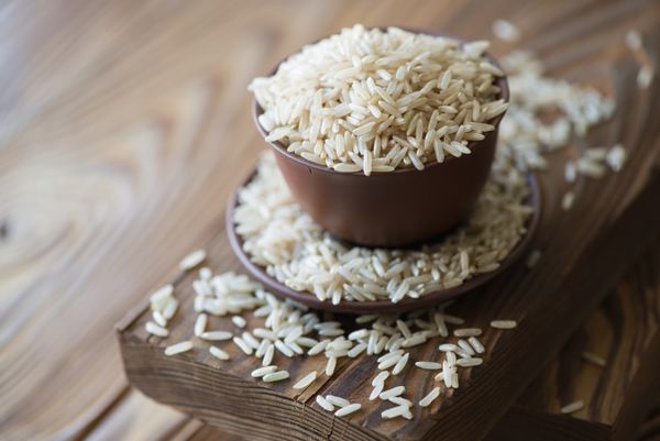 برنج قهوه ای خام در ظروف سرامیکی روی پس زمینه چوبی