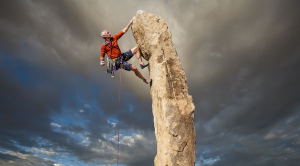کوهنورد برای گرفتن بعدی خود در لبه یک صخره چالش برانگیز تلاش می کند