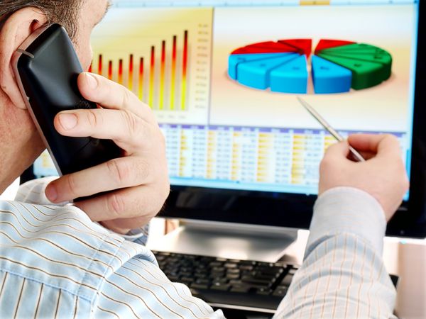 تجزیه و تحلیل داده ها در رایانه مردی روی تلفن در حال تجزیه و تحلیل داده ها و نمودارهای مالی روی صفحه کامپیوتر