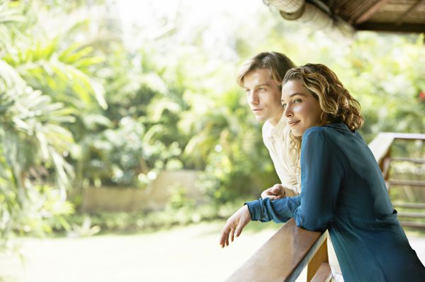 نمای جانبی یک زوج جوان در تعطیلات تکیه بر ایوان بالکن و تماشای یک باغ گرمسیری