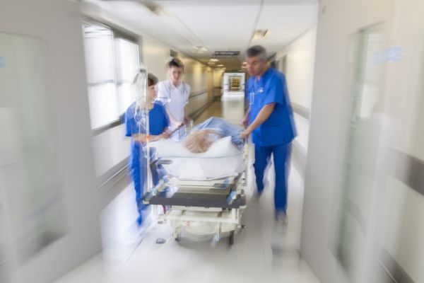 عکسی با حرکت تار از یک بیمار روی برانکارد یا گارنی که با سرعت از طریق راهروی بیمارستان توسط پرستاران پزشکان به اتاق اورژانس هل داده می‌شود