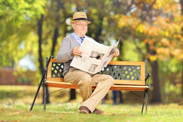 آقای ارشدی که روی یک نیمکت چوبی نشسته و در یک پارک روزنامه می خواند