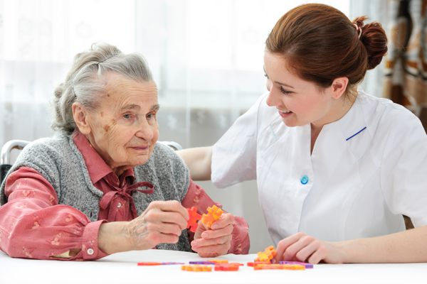 پرستار به زن سالمند کمک می کند تا پازل را در خانه سالمندان حل کند