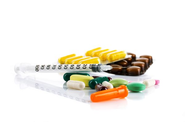 داروهای رنگارنگ در قرص ها و کپسول ها و سرنگ انسولین جدا شده روی سفید