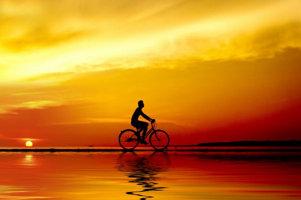 سیلوئت دوچرخه سواری که در غروب آفتاب با انعکاس می چرخد