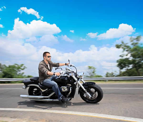 مرد جوانی سوار بر موتورسیکلت در جاده ای باز
