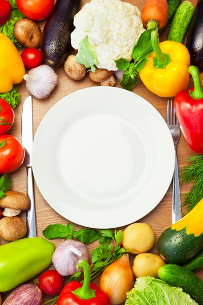 سبزیجات ارگانیک در اطراف بشقاب سفید با چاقو و چنگال