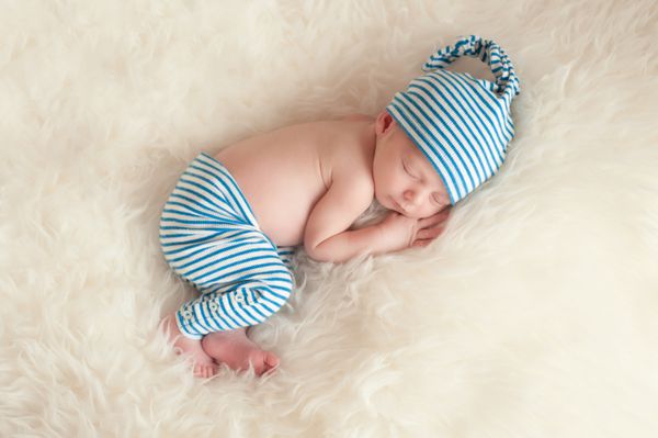نوزاد تازه متولد شده در خواب با لباس خواب و کلاه خواب