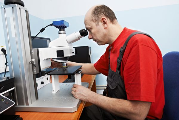 کارگر در حال بررسی پروب با میکروسکوپ صنعتی