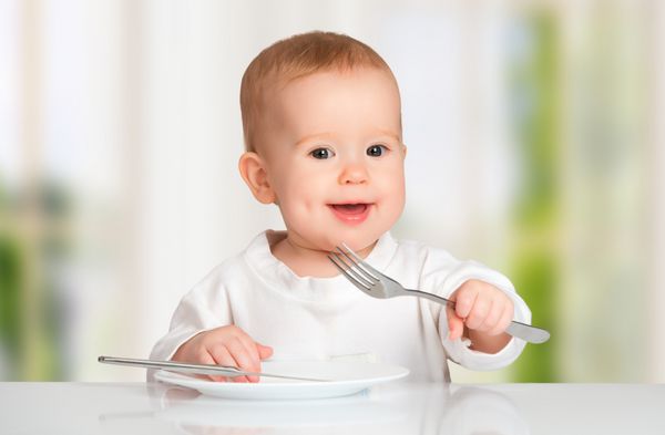 کودک بامزه با چاقو و چنگال در حال خوردن غذا