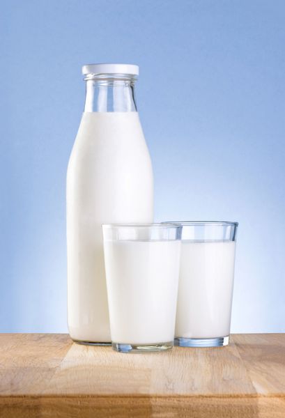 بطری کامل شیر تازه و دو لیوان میز چوبی روی بلوز است