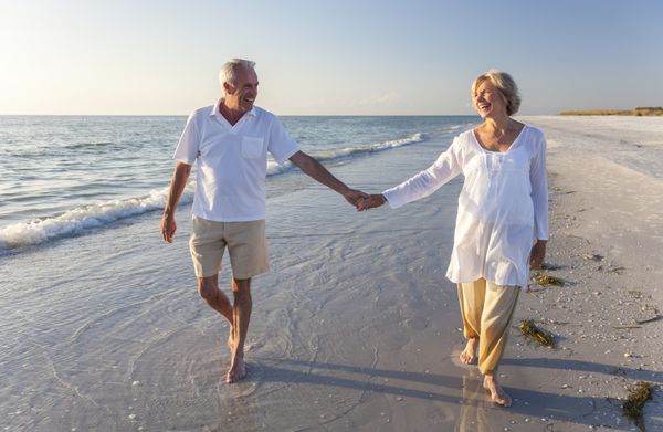 زوج سالخورده شاد که در حال قدم زدن در ساحل استوایی هستند