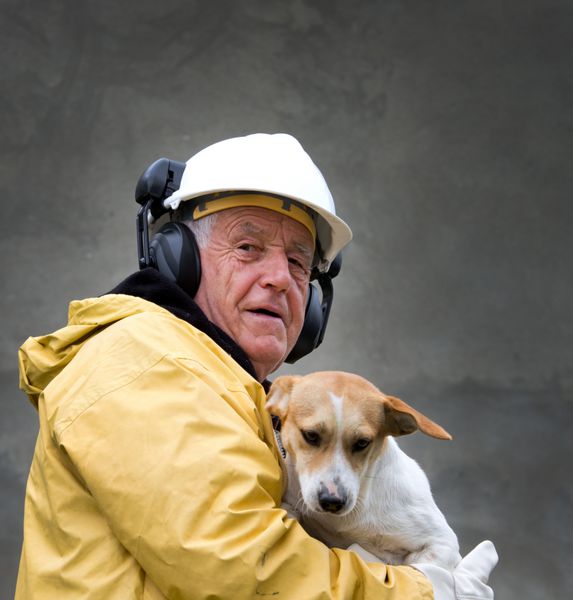 پیرمردی با لباس ایمنی سگ را در آغوش گرفته است