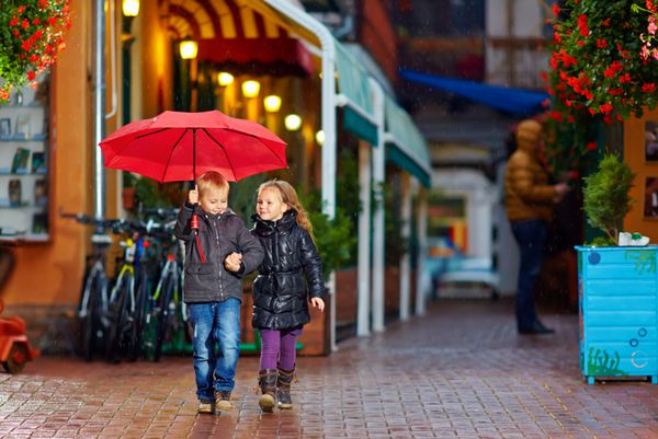 بچه های شادی که در خیابان زیر باران قدم می زنند