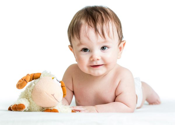 نوزاد پسر با اسباب بازی بره روی شکم دراز کشیده است