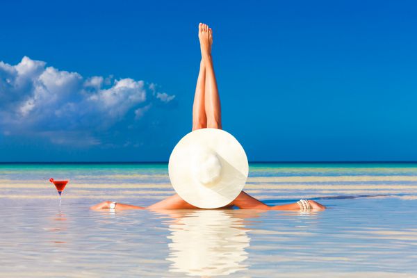 زن جوان با کلاه حصیری در ساحل استوایی دراز کشیده و لذت می برد