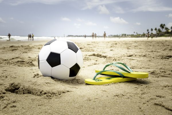 توپ فوتبال و یک فلیپ فلاپ زرد در ساحل