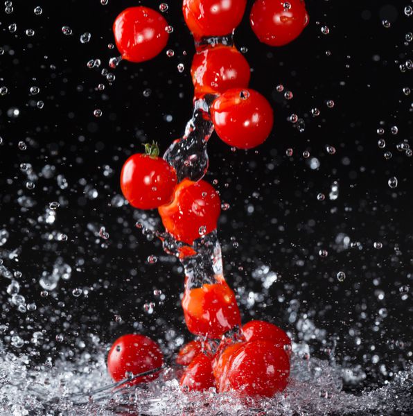 گوجه گیلاسی در آب پاشیده شده در پس زمینه سیاه
