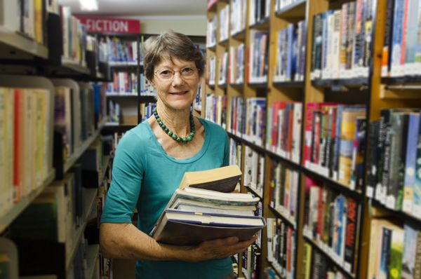 یک زن کتابدار کتاب هایی را در کنار قفسه کتاب در کتابخانه نگه می دارد