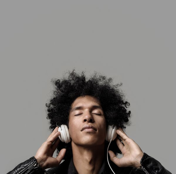مرد رترو آفریقایی در حال گوش دادن به موسیقی با هدفون دی جی با چشمان بسته جدا شده در پس زمینه خاکستری در استودیو