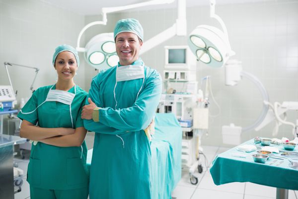 جراحان ایستاده در حالی که لبخند می زنند در سالن جراحی