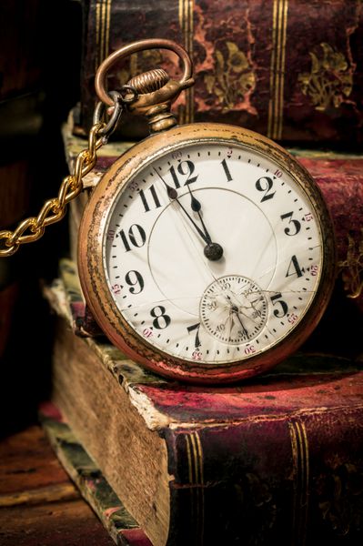 ساعت جیبی عتیقه که چند دقیقه مانده به نیمه شب را روی کتاب‌های باستانی با صدای کم نشان می‌دهد مفهوم زمان گذشته یا مهلت