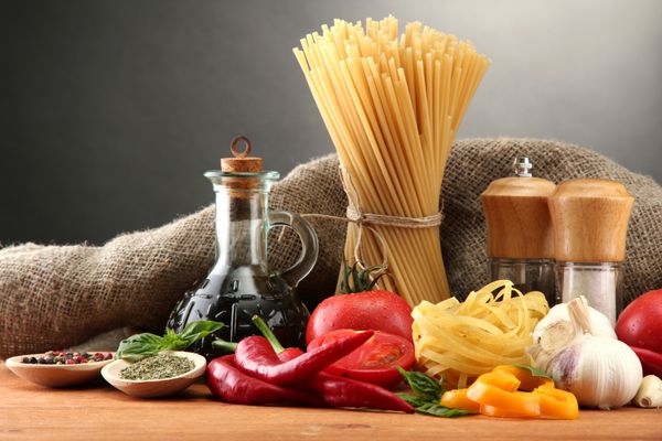 اسپاگتی پاستا سبزیجات و ادویه جات روی میز چوبی در زمینه خاکستری