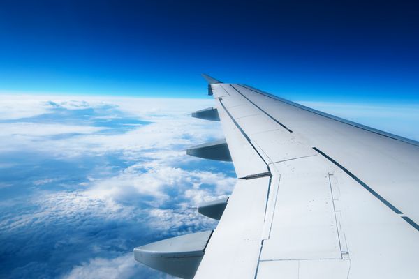 بال یک هواپیما که بر فراز ابرها پرواز می کند مردم از پنجره هواپیما به آسمان نگاه می کنند و از حمل و نقل هوایی برای سفر استفاده می کنند