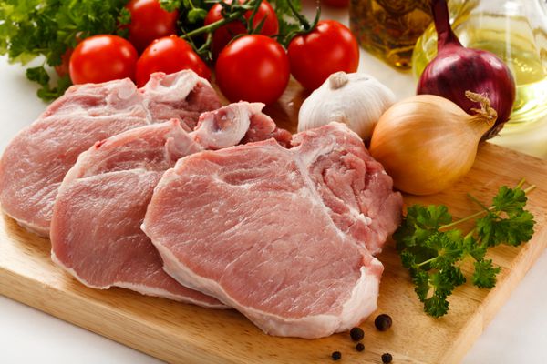 گوشت خوک خام روی تخته برش و سبزیجات