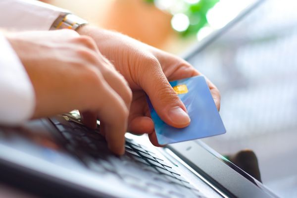 تاجر جوانی که یک کارت اعتباری در دست دارد و در حال تایپ کردن است خرید آنلاین از طریق اینترنت با استفاده از لپ تاپ