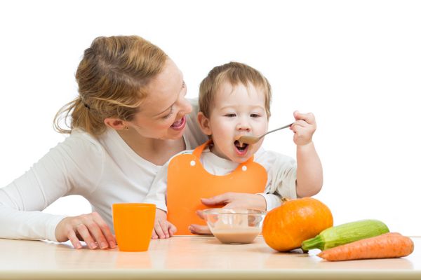 کودک در حال خوردن پوره سبزیجات با قاشق و نشستن روی آغوش مادر