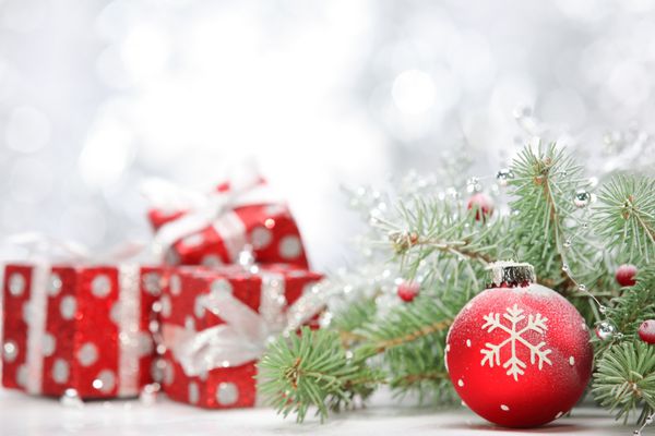 نمای نزدیک از توپ کریسمس با شاخه کاج و هدایایی در پس زمینه انتزاعی