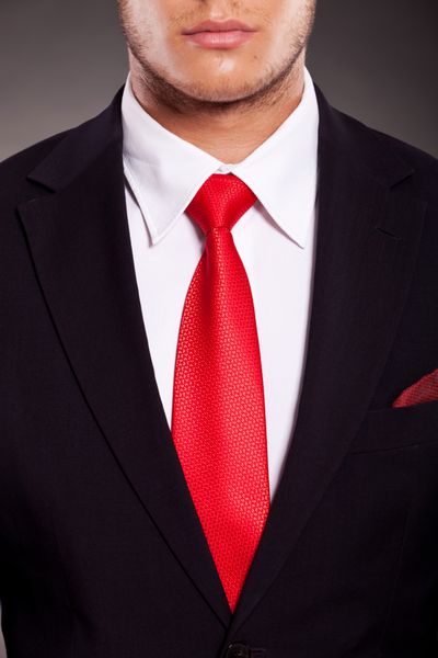 جزئیات کت و شلوار مرد جوان تجاری با کراوات قرمز در پس زمینه تیره