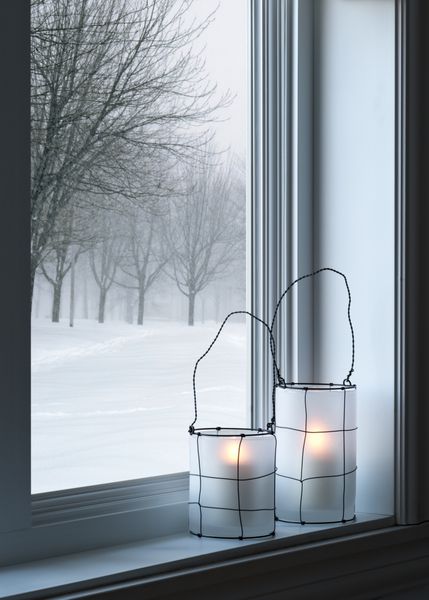 فانوس های دنج روی طاقچه با چشم انداز زمستانی که از پنجره دیده می شود