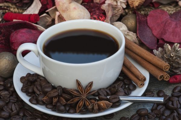 فنجان قهوه در پس زمینه کریسمس با دارچین بادیان ستاره ای و دانه های قهوه