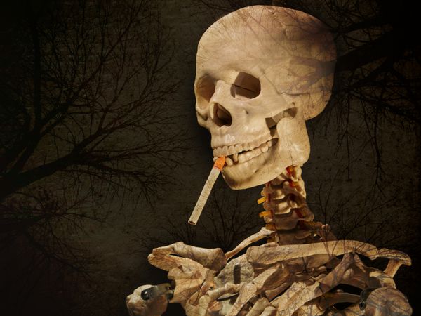 تصویر ترسناک انتزاعی از اسکلت و جمجمه جعلی در حال کشیدن سیگار لایه لایه با گرافیک گرانج درخت مرده که ظاهری ترسناک دارد