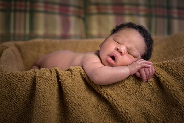 پسر بچه آمریکایی آفریقایی-آمریکایی تازه متولد شده از نزدیک در سبد خوابیده با پتوی قهوه ای عمق میدان کم