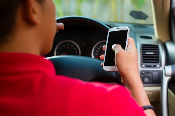 مرد آسیایی نشسته در ماشین با تلفن همراه در دست هنگام رانندگی پیامک می دهد
