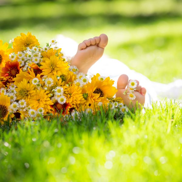 پای کودکان روی گل بهاری در پس زمینه چمن سبز