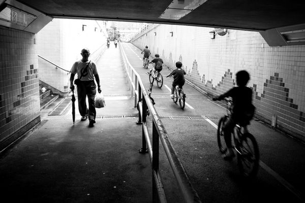 تصویری از بچه های دوچرخه سوار و پدر و پیرمردی که در انتهای تونل قدم می زنند با نور پس زمینه در خیابان هنگ کنگ
