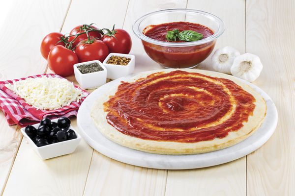 رب گوجه فرنگی روی خمیر پیتزا خام با پنیر رنده شده زیتون سیاه سس گوجه فرنگی و گوجه فرنگی پخش شده است