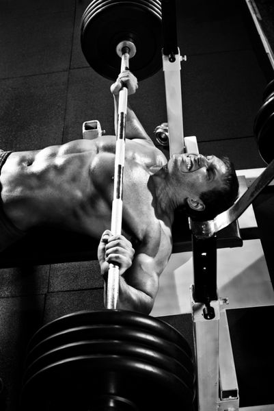 مرد ورزشکار بسیار قدرتمند اجرای پرس ورزشی با وزنه در سالن ورزشی پو سیاه و سفید