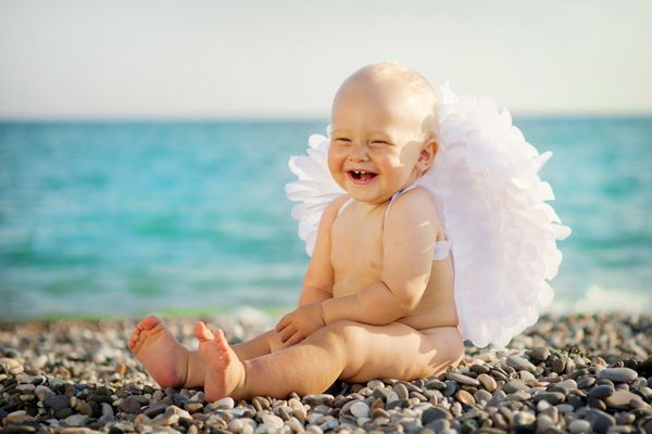 کودک ناز با بال های فرشته در ساحل نشسته است