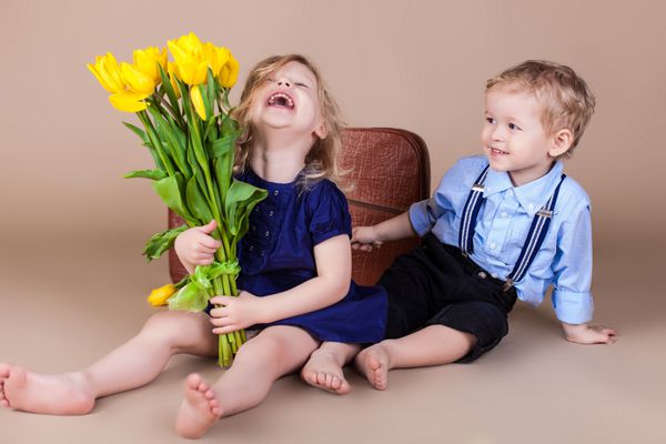 بچه های بامزه پسر کوچولوی شادی که یک دسته گل دختر ناز از گل های زرد بهاری می دهد سریال در استودیو روز