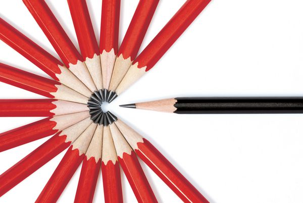 نمای نزدیک از یک مداد سیاه که از دایره ای که توسط نوک چند مداد قرمز تشکیل شده است برجسته شده است جدا شده روی سفید