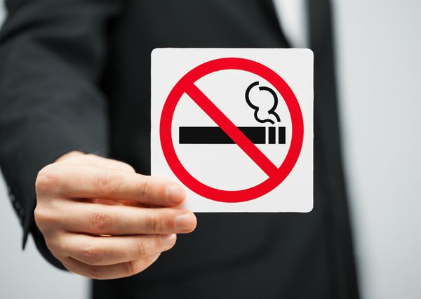 تصویر مردی با کت و شلوار که تابلوی سیگار ممنوع در دست دارد