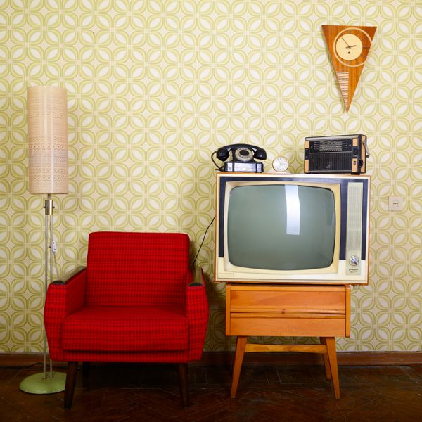اتاق قدیمی با کاغذ دیواری صندلی راحتی قدیمی تلویزیون رترو تلفن ساعت پخش کننده رادیو و لامپ استاندارد